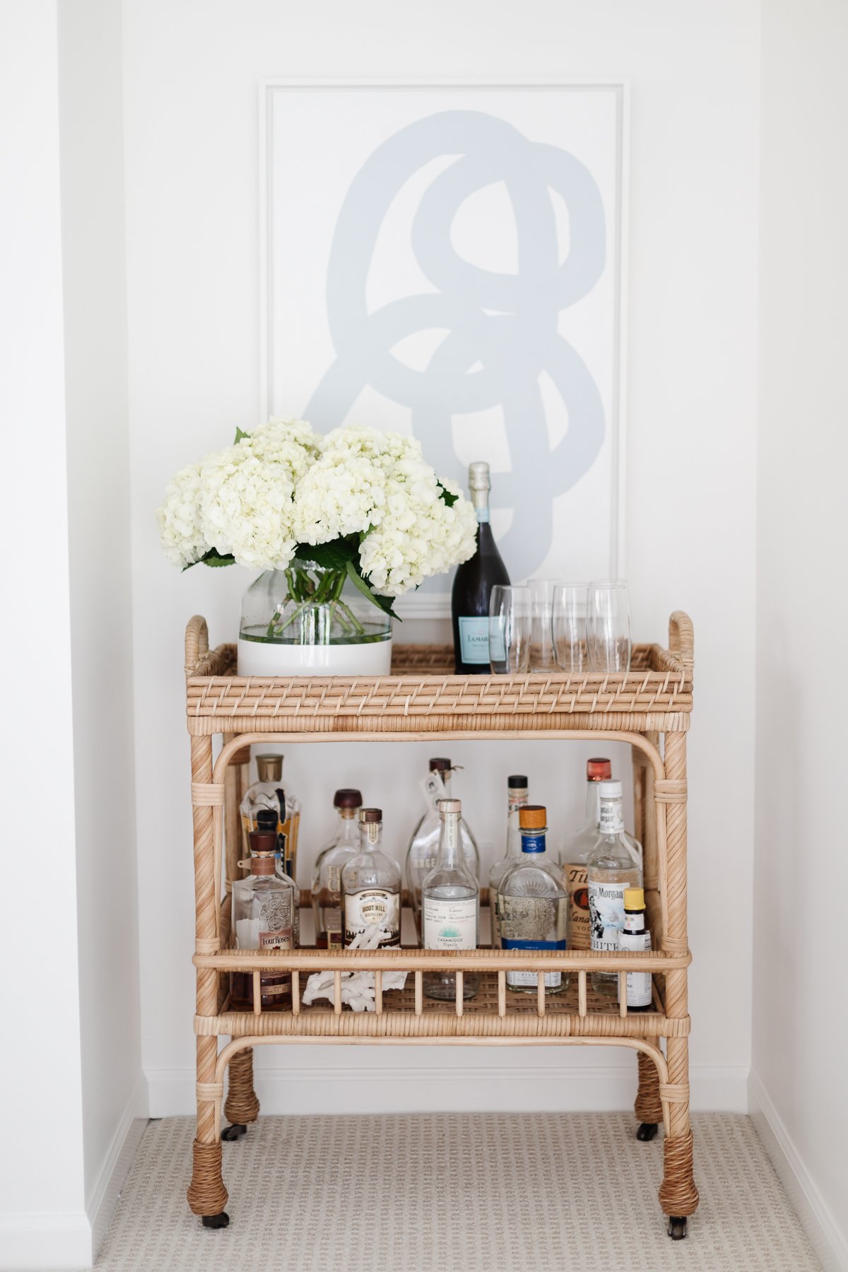 A rattan bar cart with a vase of fresh flowers and modern art behind it. 