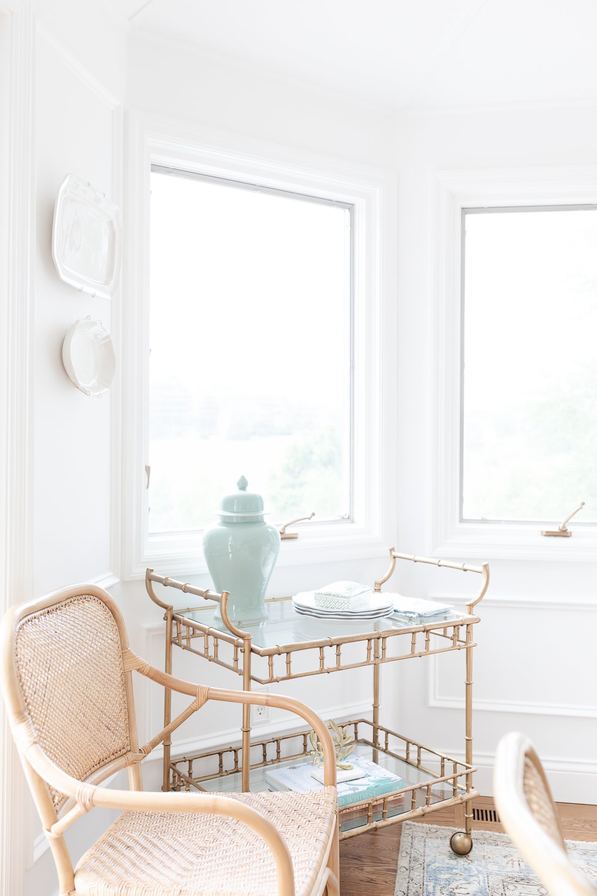 A bar cart styled without alcohol in a white dining room with a wood table.