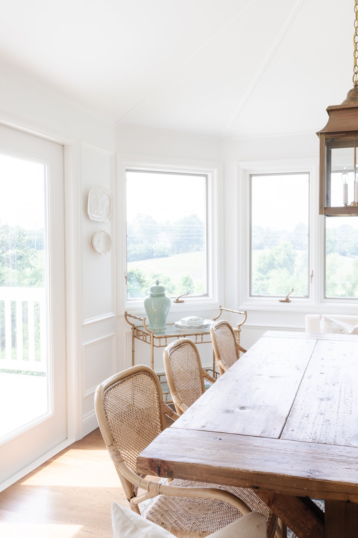 A bar cart styled without alcohol in a white dining room with a wood table.