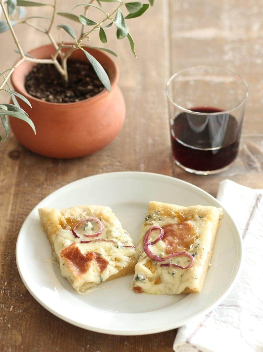 prosciutto pizza on white plate with wine and olive plant