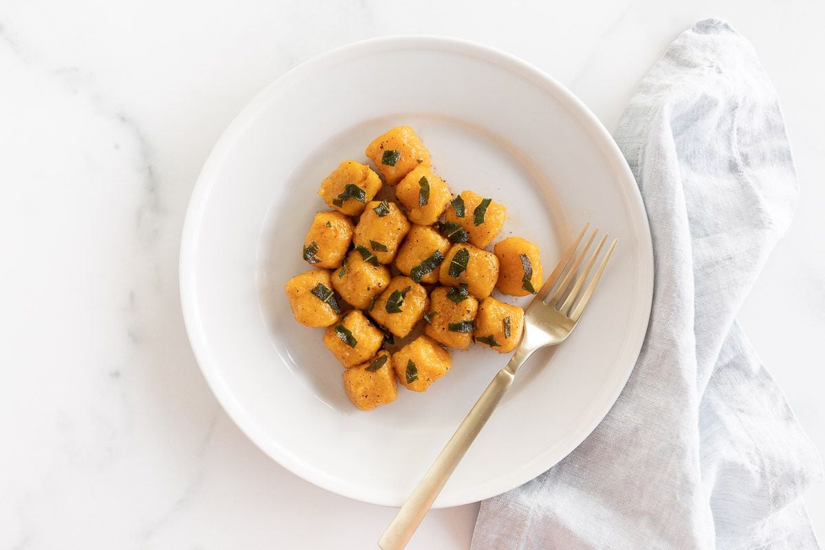 A white plate with sweet potato gnocchi and a gold fork