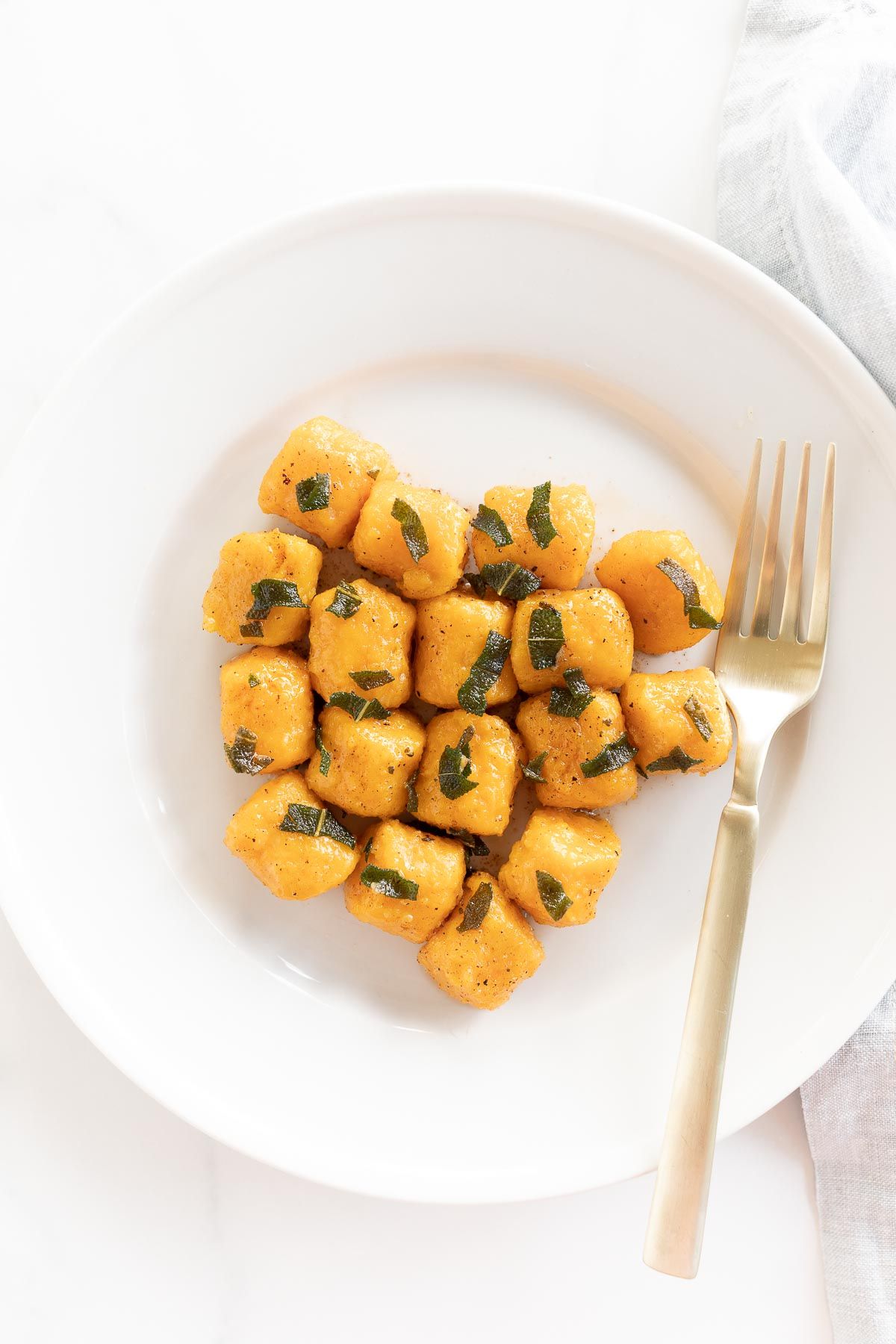 A white plate with sweet potato gnocchi and a gold fork