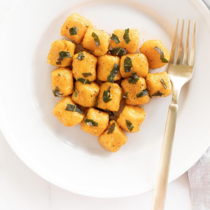 A white plate with sweet potato gnocchi and a gold fork