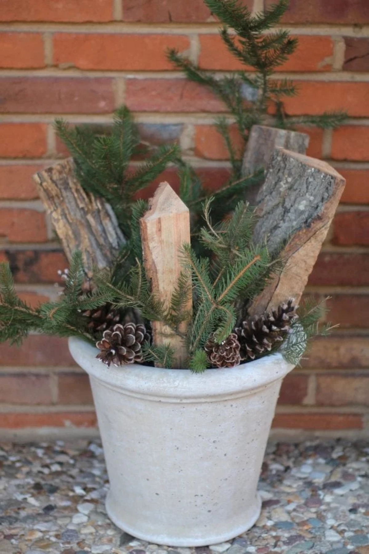 A winter planter for front porch with cut firewood, evergreens, pine cones