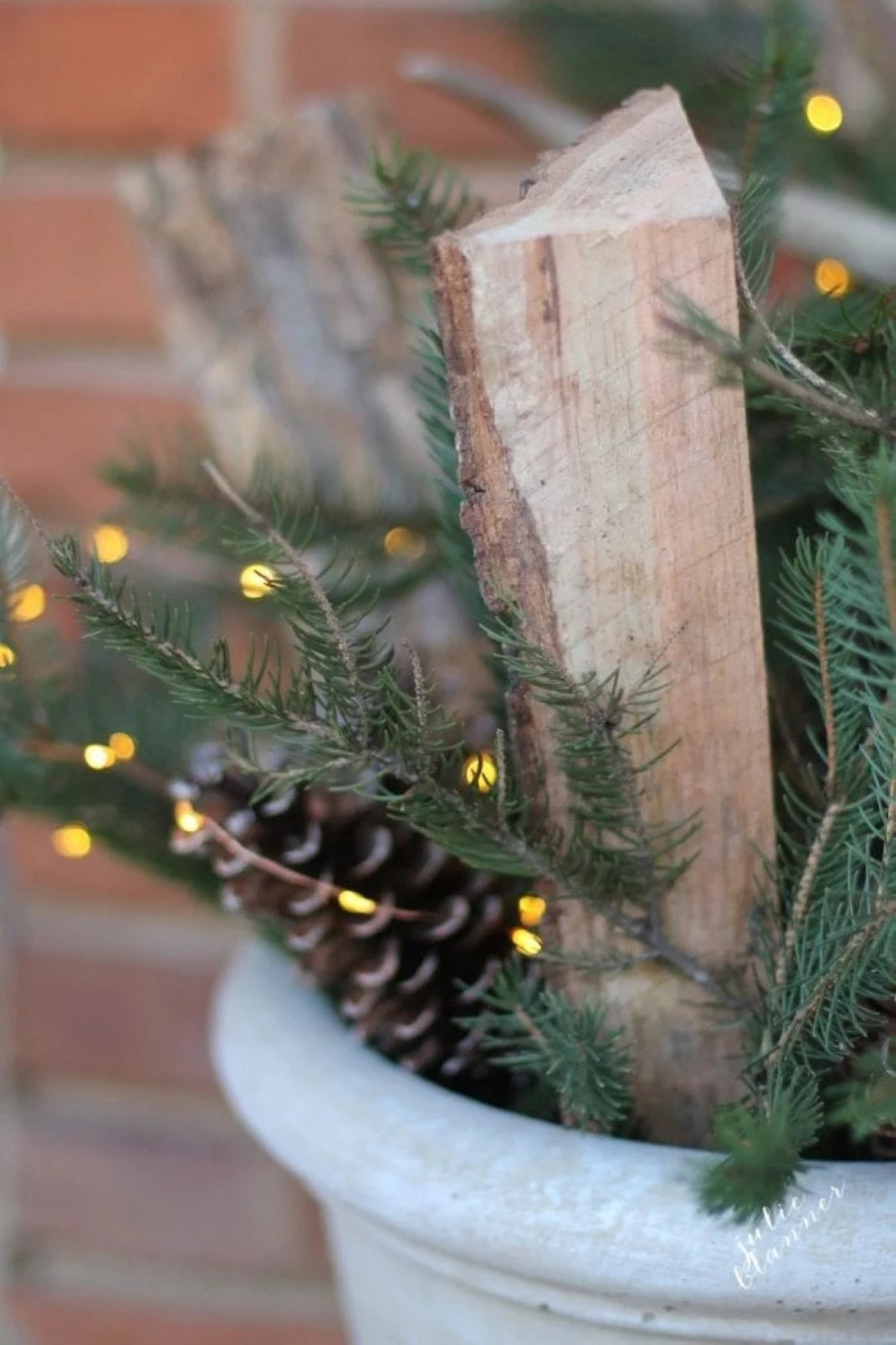 A winter planter for front porch with cut firewood, evergreens, pine cones and fairy lights