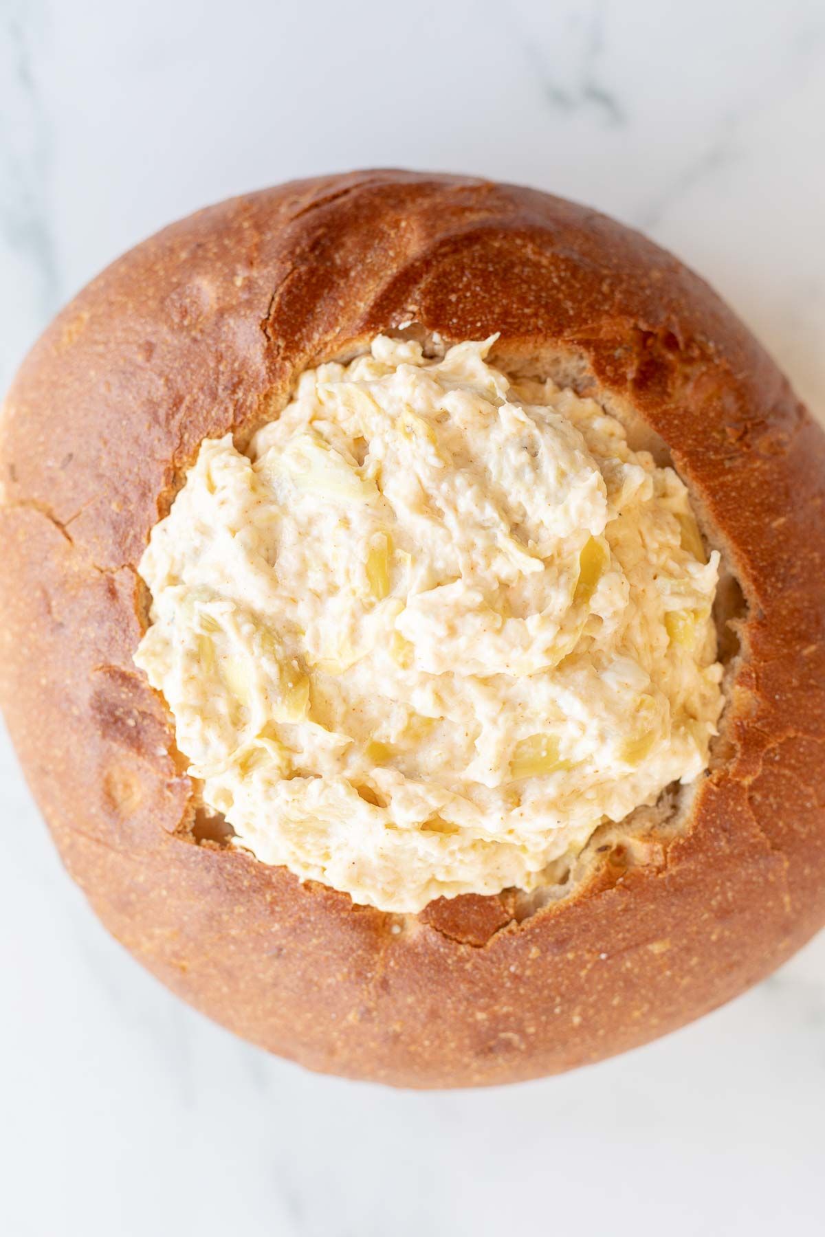 A bread bowl filled with artichoke dip