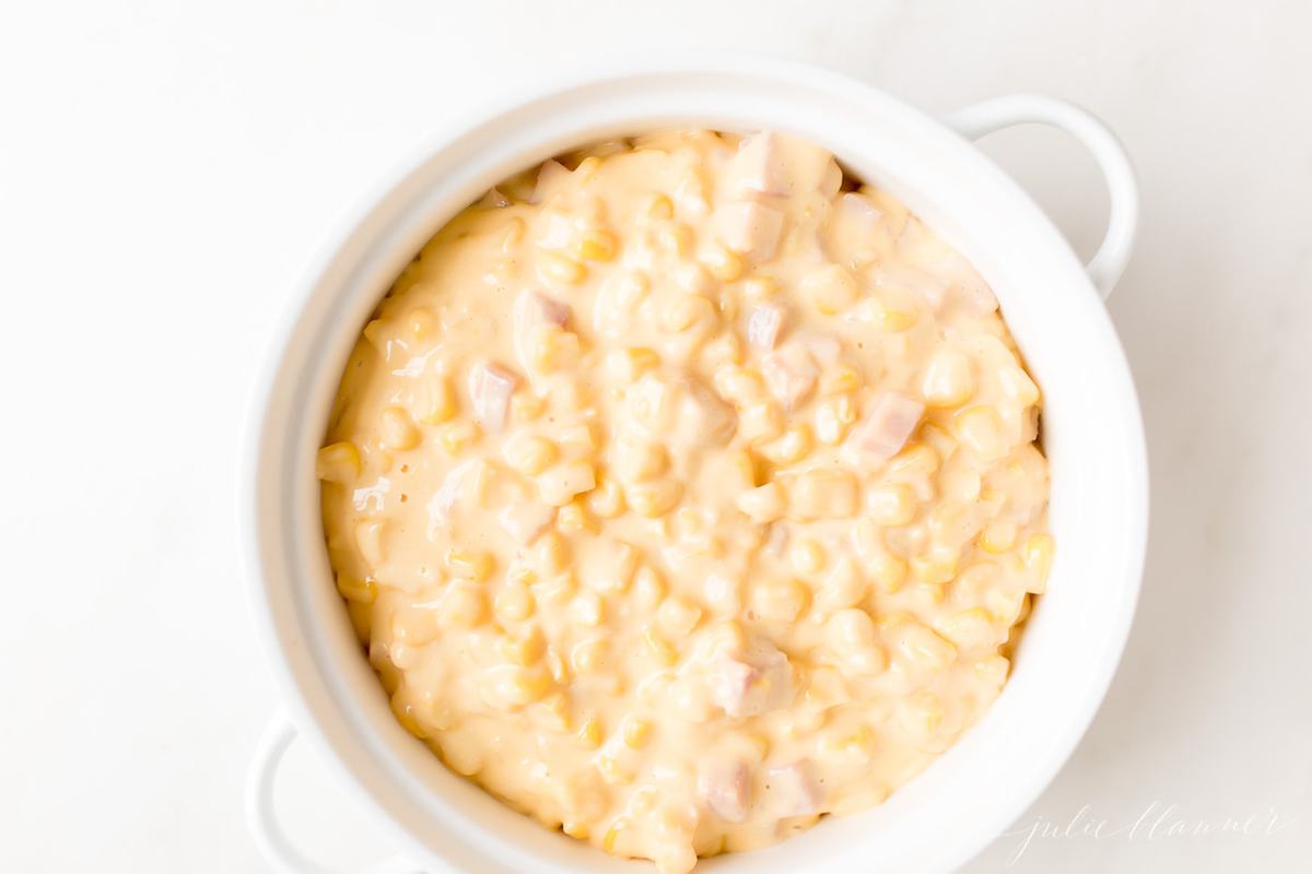 A white casserole dish with handles, filled with cheesy corn dip.