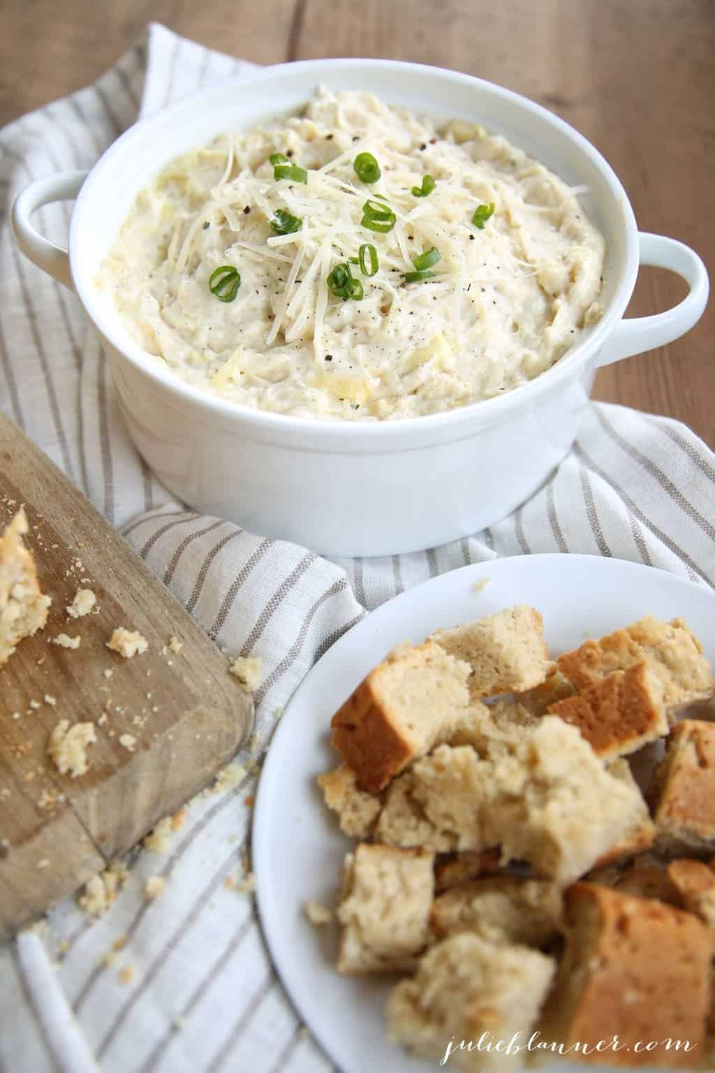 A white dish full of artichoke dip with chunks of bread to the side.