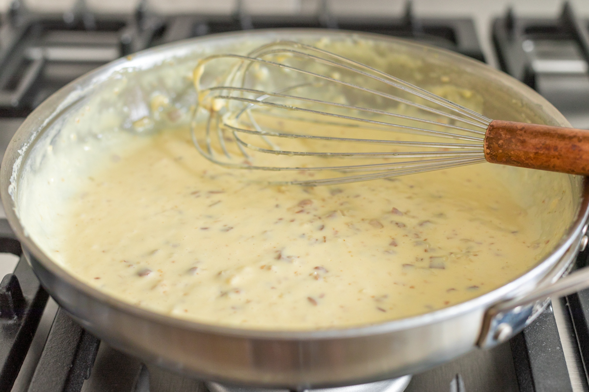 Cheese sauce in a pot on a stovetop with a whisk.