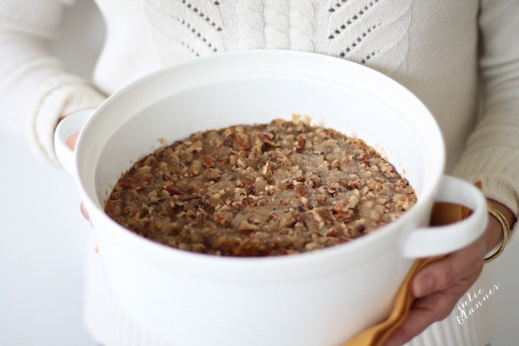 Sweet Potato Casserole with pecans in a white pot, held by a woman in a white sweater.
