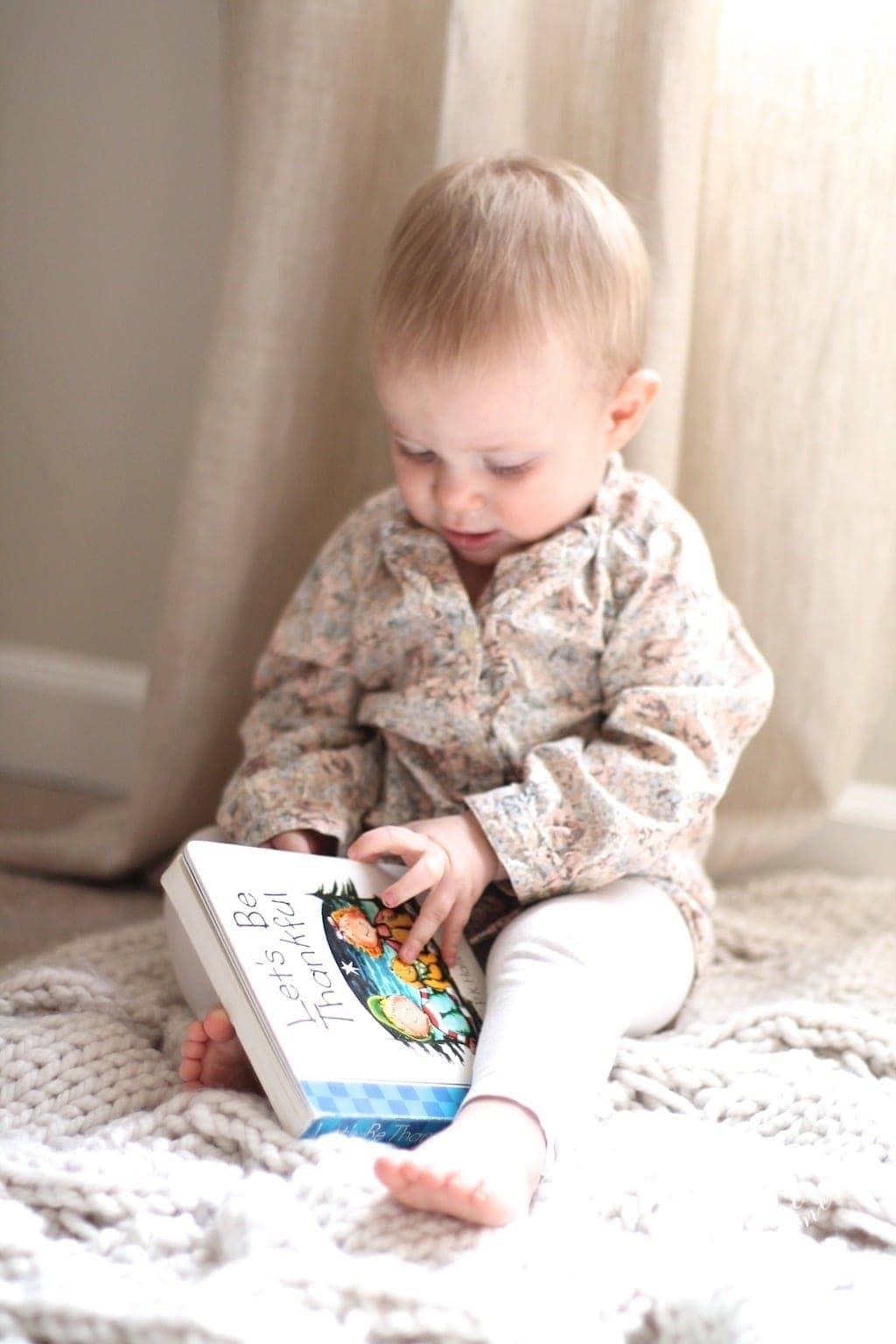 A little blonde toddler reading a Let's be Thankful book.