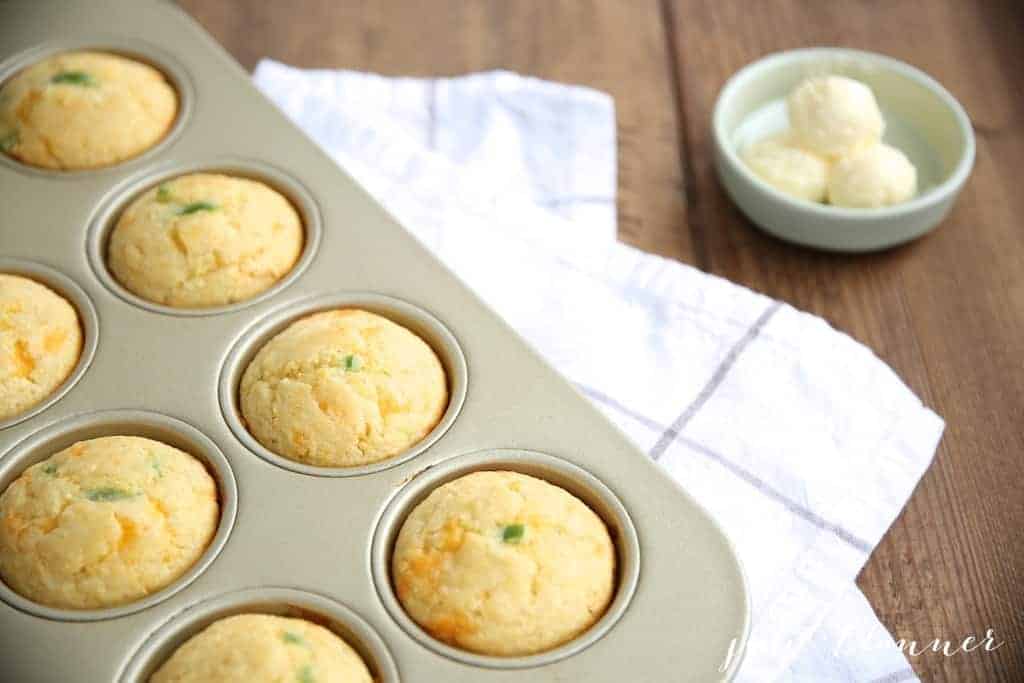 A muffin pan filled with cornbread muffins, pats of butter to the side
