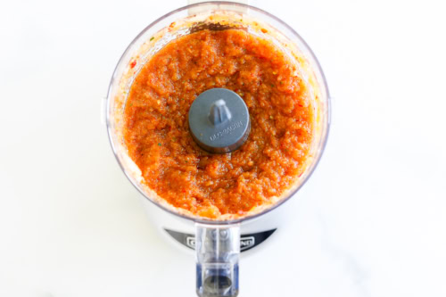 Top view of a food processor containing freshly made chipotle vinaigrette on a white background.