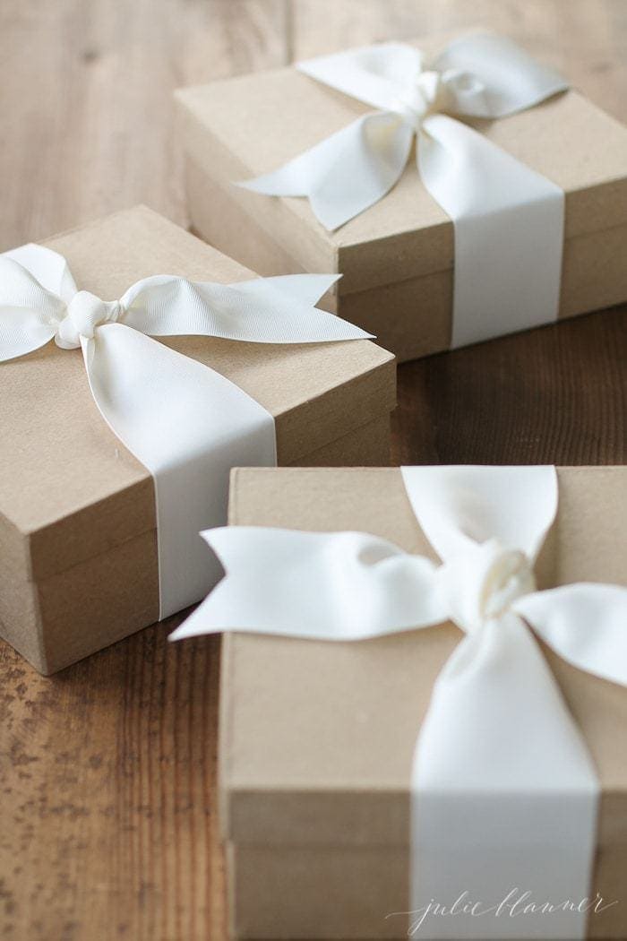 three kraft paper boxes tied with cream ribbon bows on a wood surface.
