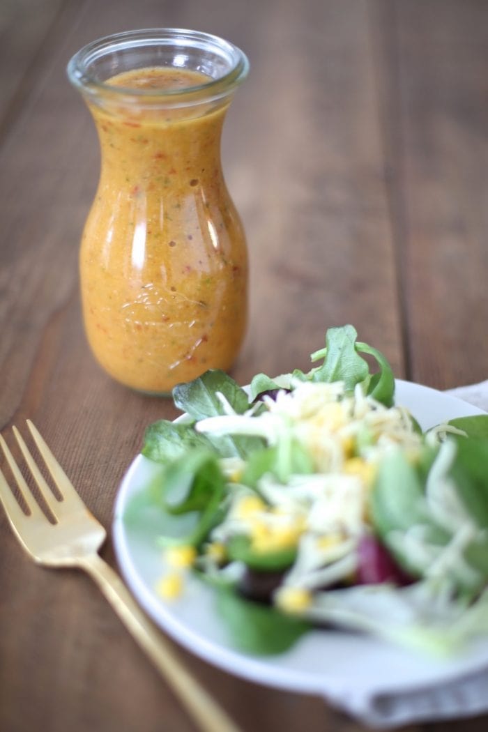 apple chipotle salad dressing in glass bottle with salad on white plate and gold fork