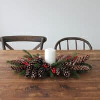 A berry and pinecone centerpiece with a candle in the middle on a farm table.