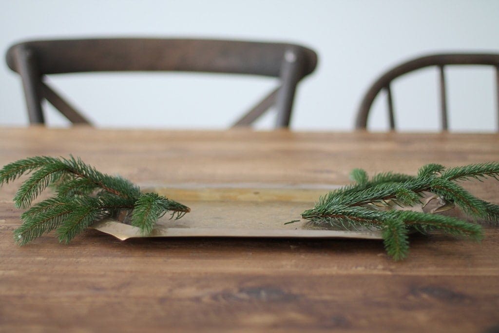 A gold tray with holiday greenery on the sides on a farm table.