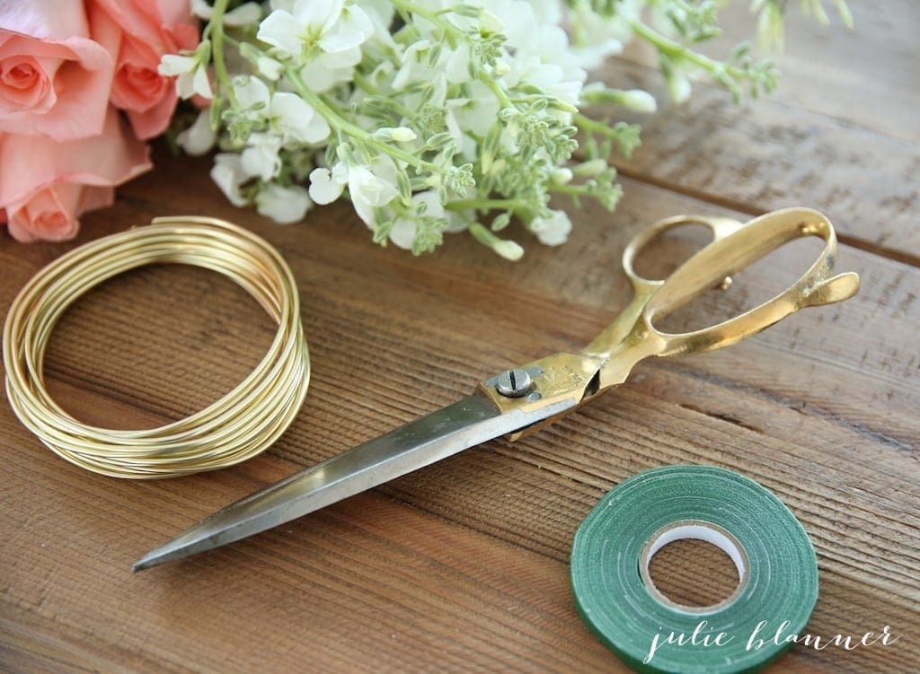 Fresh flowers, gold wire, scissors and floral tape laid out on a wooden table.