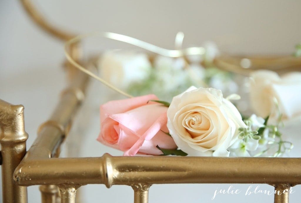 A brass and glass table with pink and white roses on flower crowns on top.