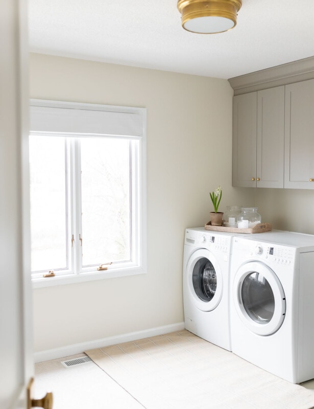 cream and gray laundry room with brass flush mount light