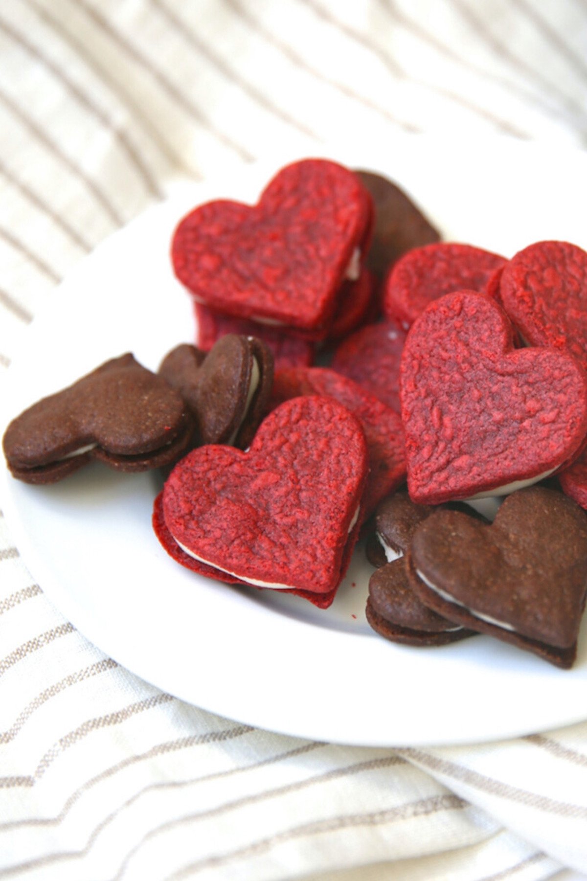 Homemade heart-shaped cookies resembling oreos are beautifully arranged on a plate.