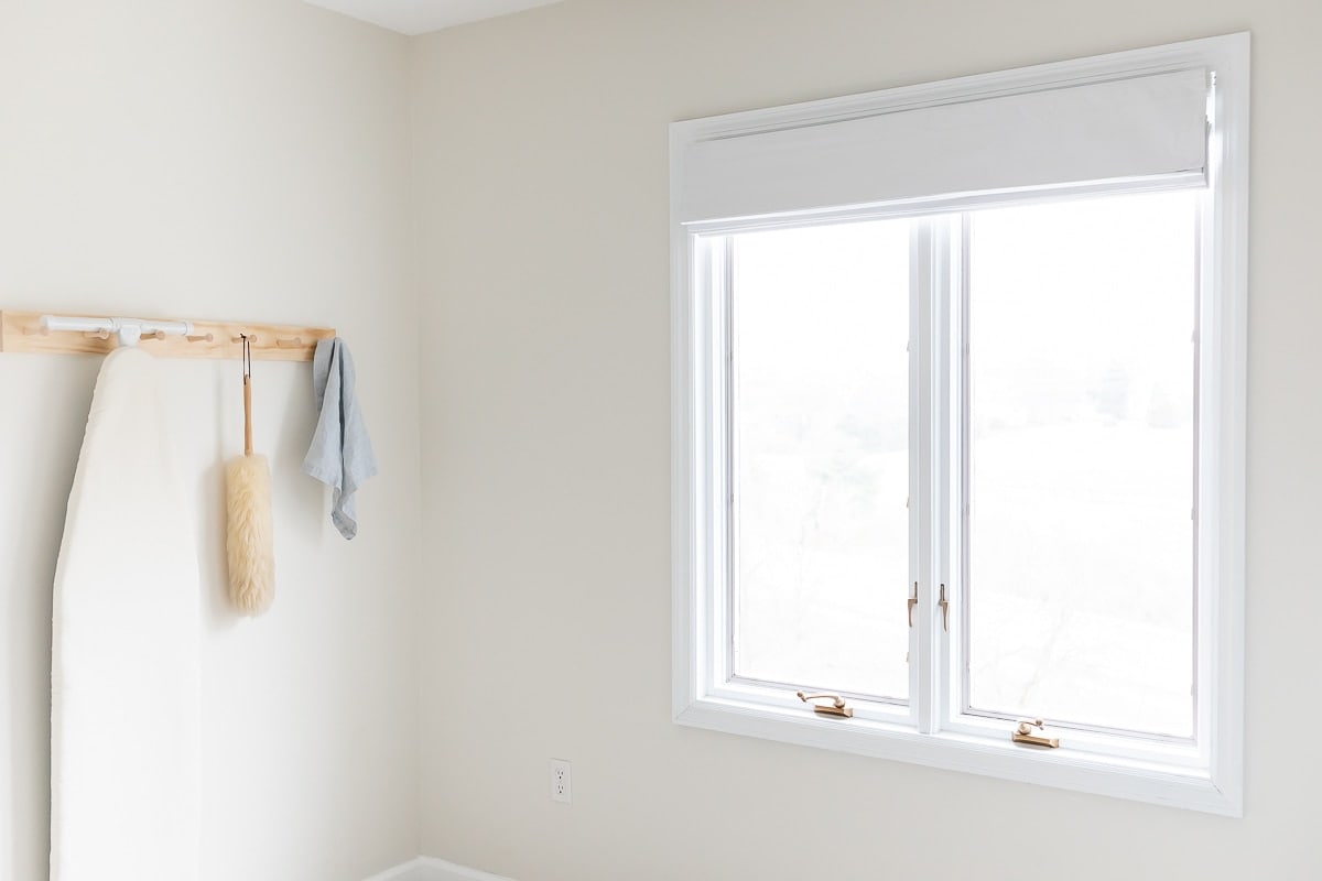 white roman shade on window next to peg rail laundry room storage