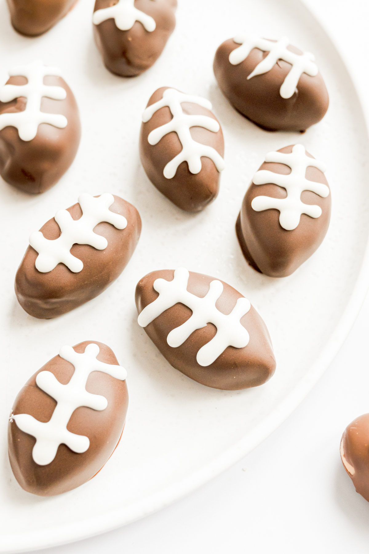 Peanut butter truffles shaped like footballs are elegantly arranged on a pristine white plate.