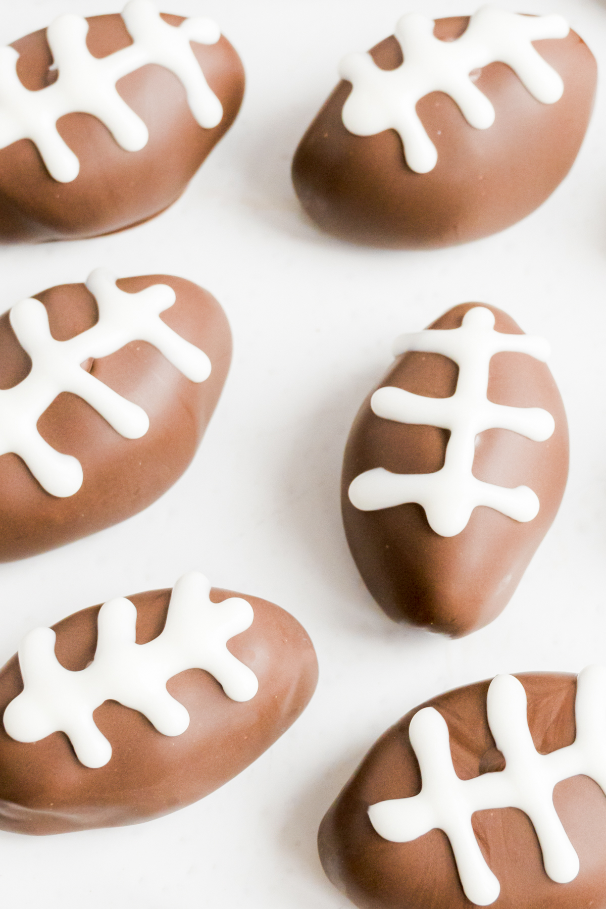 Peanut butter truffles shaped like footballs with white icing on a white surface.