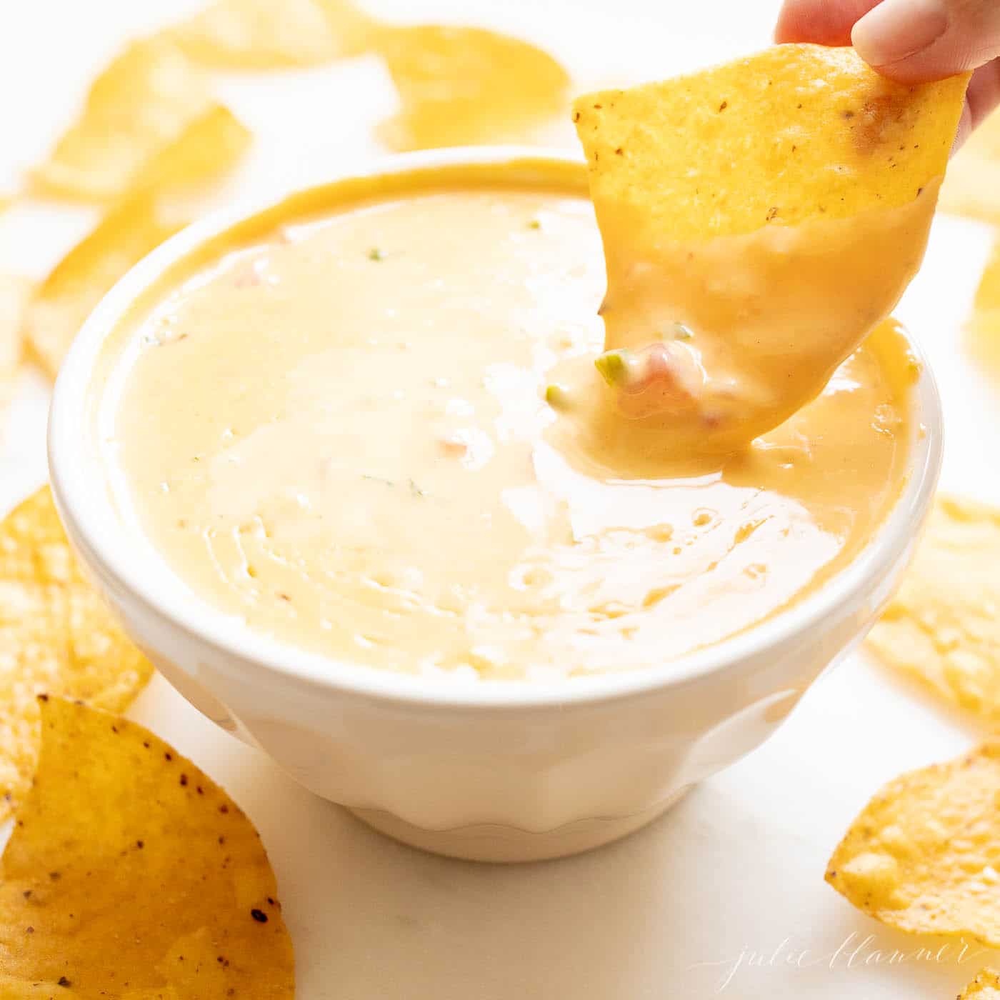 dipping a chip into a white bowl filled with velveeta cheese dip