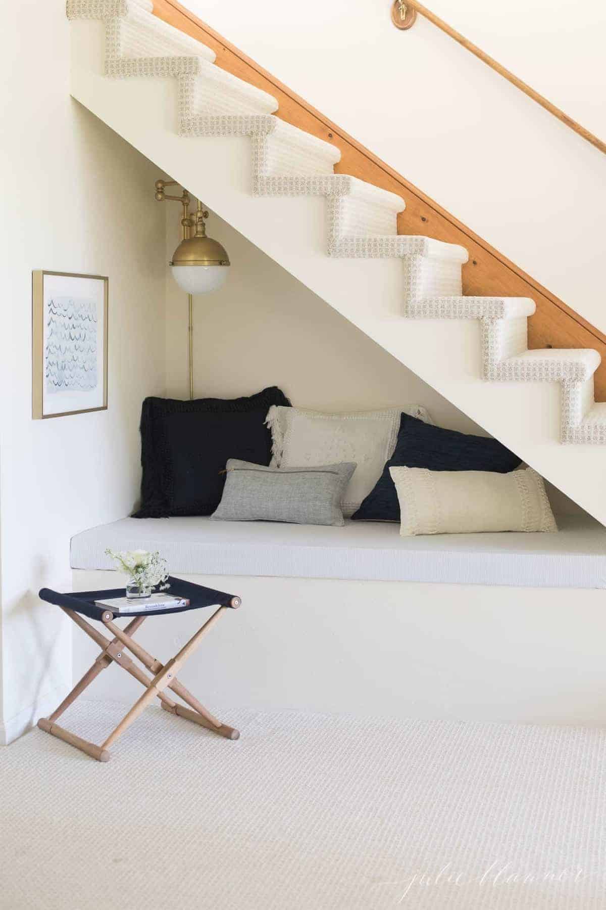 A small nook under the stairs of a lake house with a brass wall sconce.