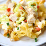 A plate of Italian chicken nachos garnished with melted cheese, green onions, and diced tomatoes.