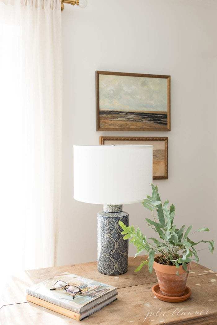 plant lamp books on antique table with painted art and curtains in background