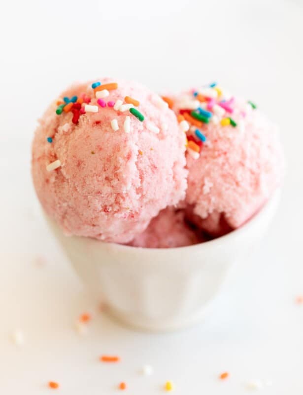 A white bowl of strawberry snow ice cream topped with rainbow sprinkles.