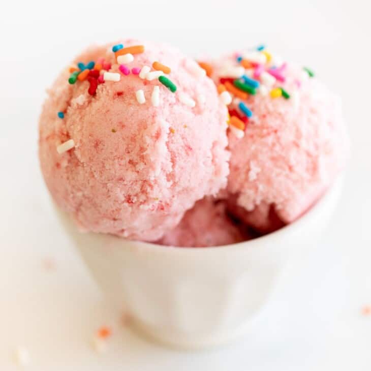 A white bowl of strawberry snow ice cream topped with rainbow sprinkles.