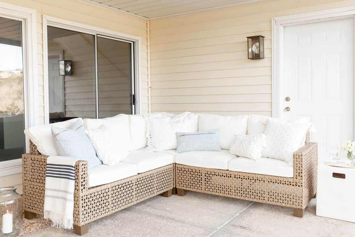 A patio with an under deck drainage system above, with a white rattan sectional.