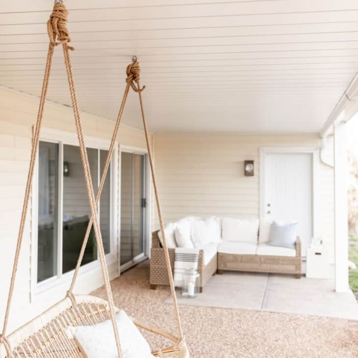 An outdoor room with a white under deck ceiling, rattan swing and sectional sofa as focal points.
