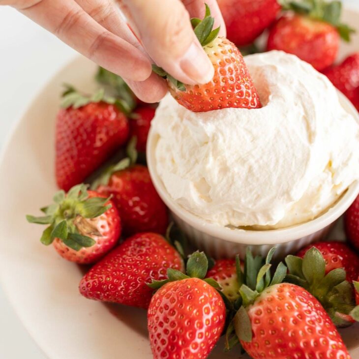 A white plate full of strawberries and a bowl of mascarpone fruit dip in the center.