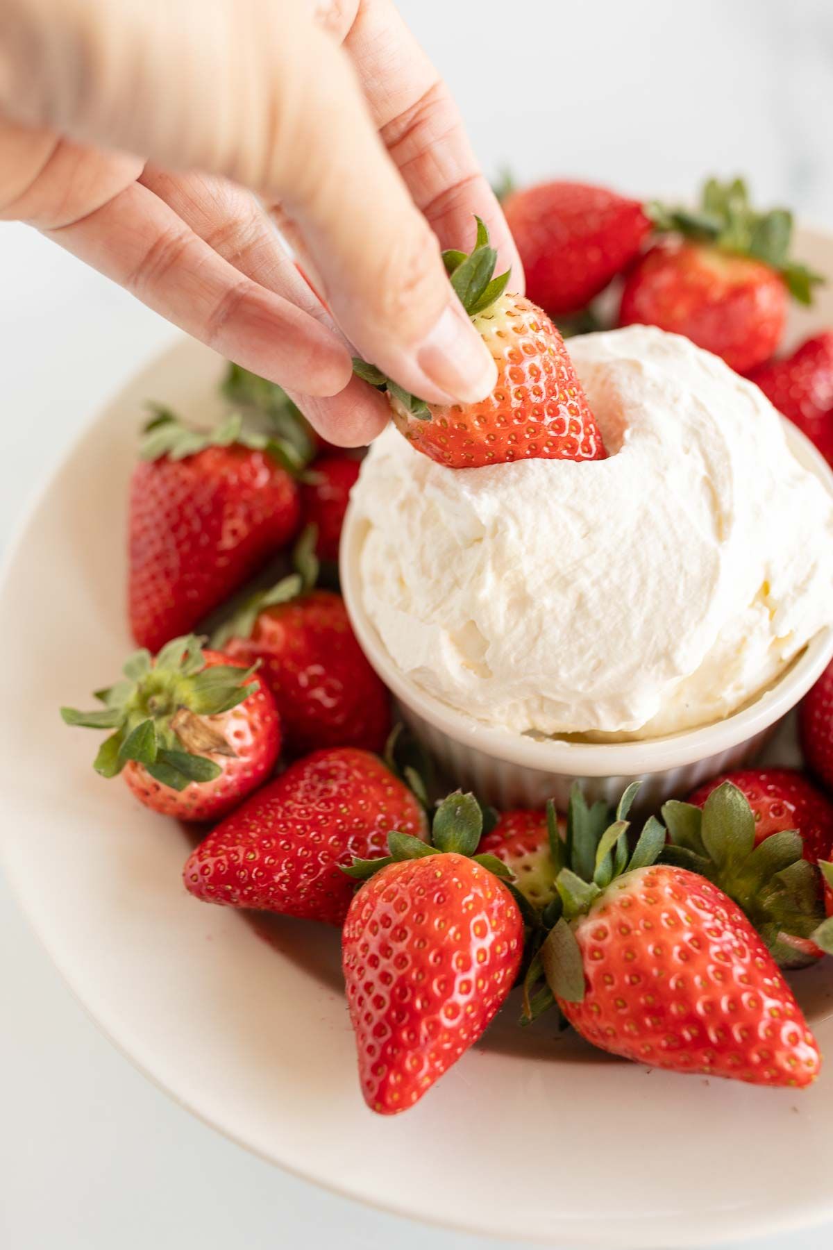 A white plate full of strawberries and a bowl of mascarpone fruit dip in the center.