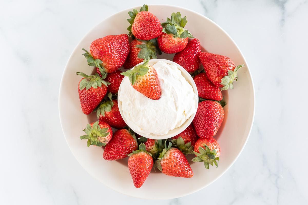 A white plate full of strawberries and a bowl of mascarpone dip in the center.