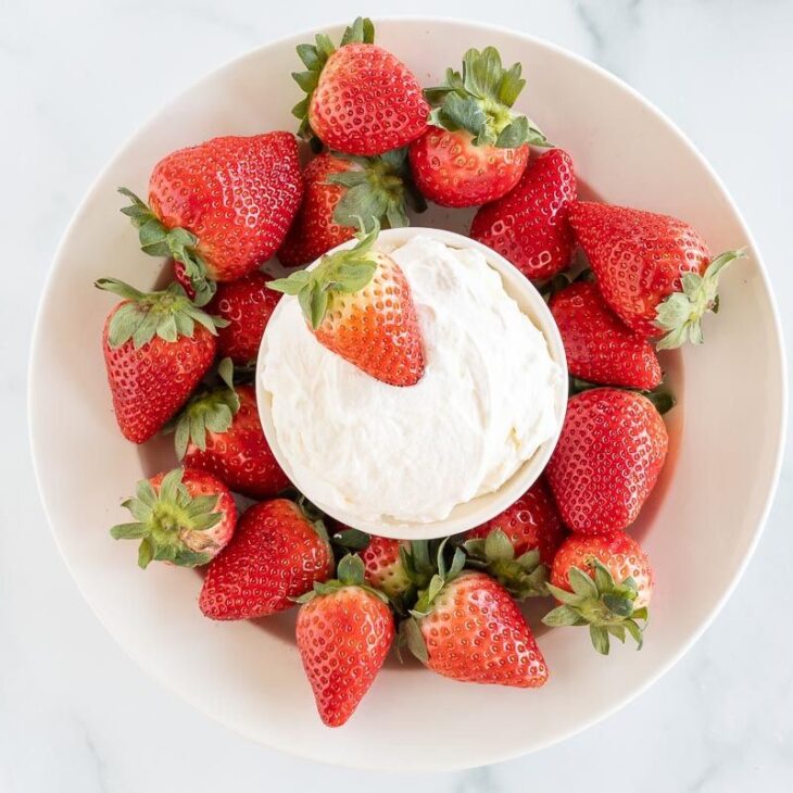 A white plate full of strawberries and a bowl of mascarpone dip in the center.