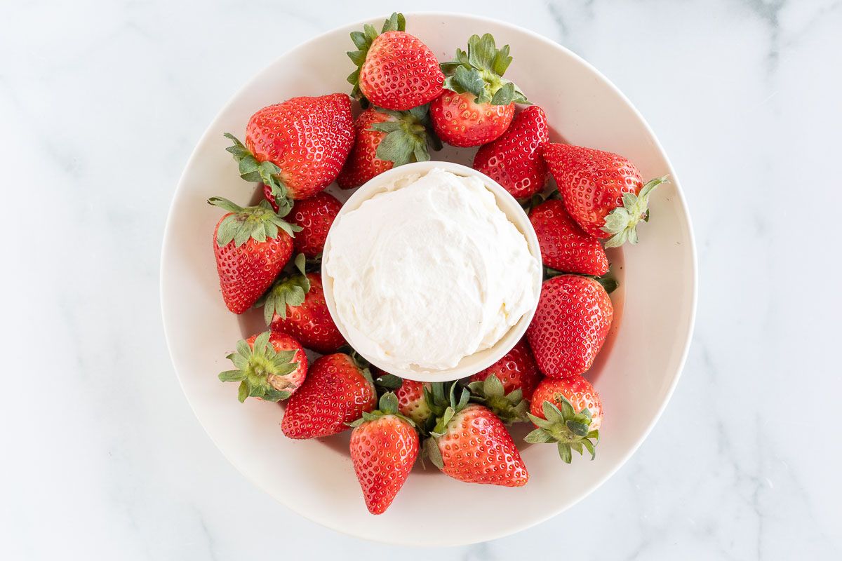 A white plate full of strawberries and a bowl of mascarpone fruit dip in the center.