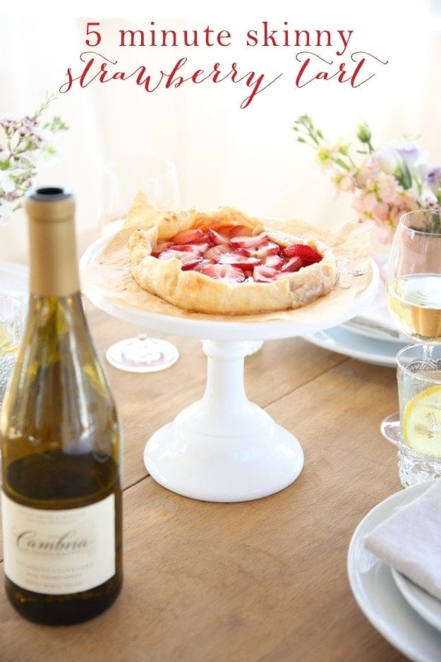 A strawberry tart on a cake stand next to a bottle of wine