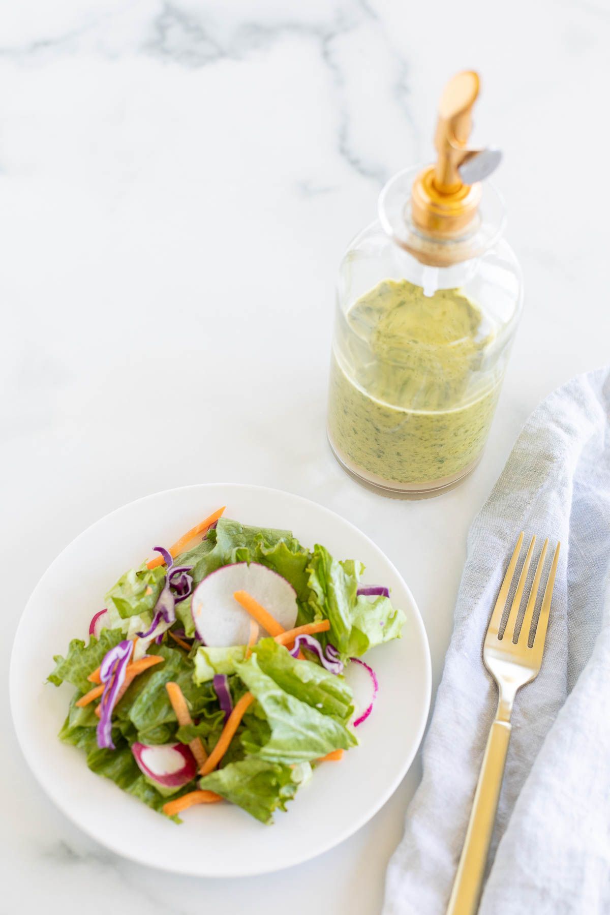 A small green salad on a white plate, with a bottle of cilantro lime vinaigrette behind it.