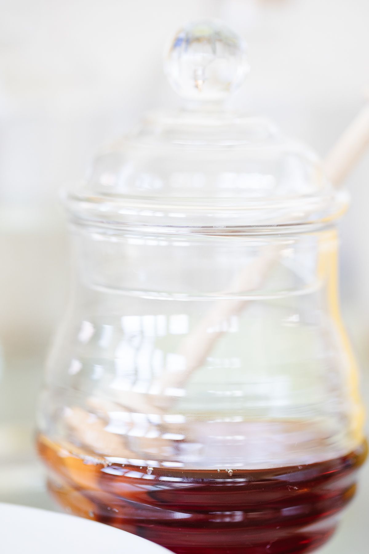 A glass jar of honey with a wooden honey server