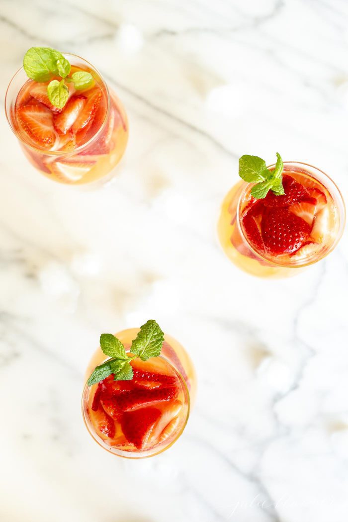 3 glasses of peach sangria topped with strawberries and garnished with mint