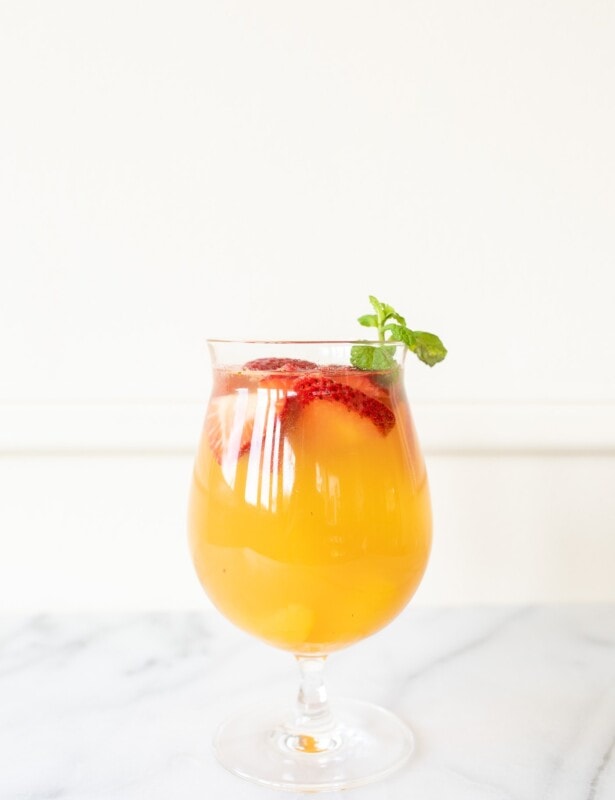 Peach Sangria in a glass, garnished with peaches, strawberries, and mint.