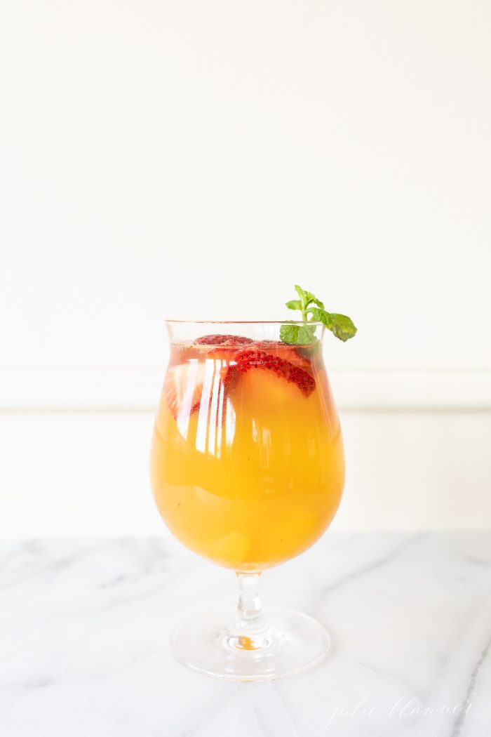 Peach Sangria in a glass, garnished with peaches, strawberries, and mint.