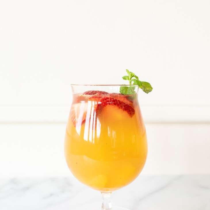 Peach Sangria in a glass, garnished with peaches, strawberries, and mint.