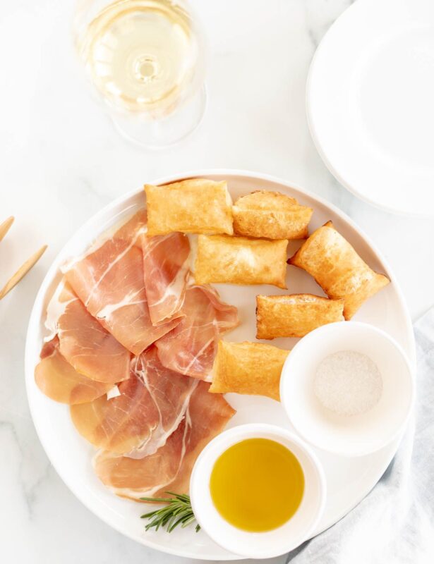 Gnocco fritto on a white plate with bowls of olive oil and sea salt to the side