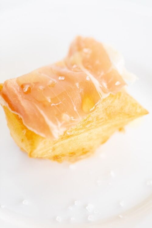 A single gnocco frito on a white plate, topped with proscuitto